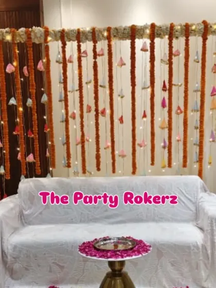 A traditional backdrop for a home kirtan. The decor consists of a seating area with a backdrop of marigold and bell strings, illuminated with fairy lights.