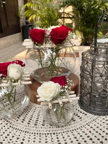 For this Christmas-themed setup, I used glass bowls with red and white roses. The simple bamboo grid on top is a 'best out of waste' idea that adds a rustic, structural element to the fresh flower arrangements.