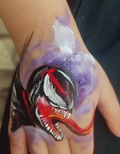 A close-up of a Venom hand tattoo. The use of purple and white highlights against the black base creates a striking, comic-book style effect.