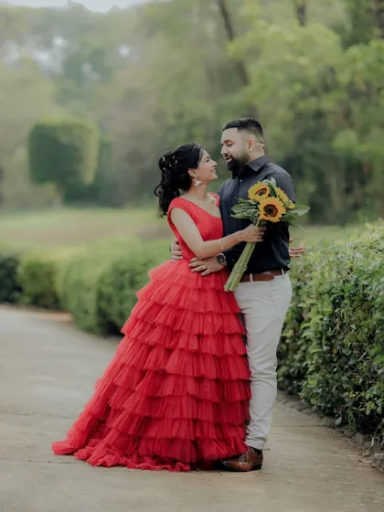 A beautiful pose during a pre-wedding session in a Pune garden. The woman's vibrant red dress stands out against the green foliage, creating a visually stunning and romantic photograph.