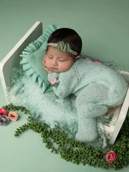 A top down view of the miniature bed setup, showing the baby surrounded by a garland of leaves and flowers, as if sleeping in a magical garden.