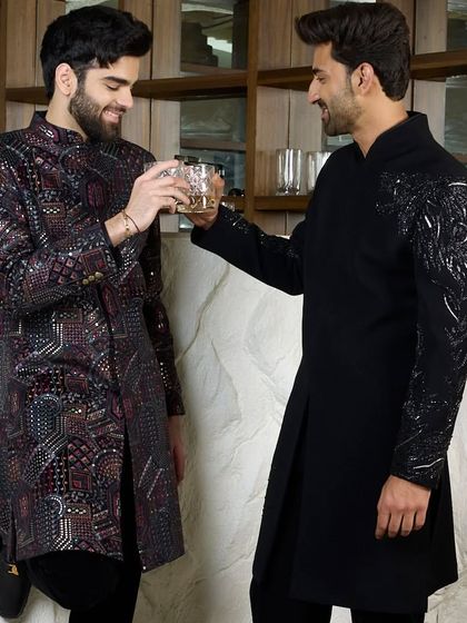 Two gentlemen sharing a toast, both in my bespoke black kurtas. One features the embroidered cheetah, while the other has a complex geometric pattern, showcasing different ways to express evening elegance.