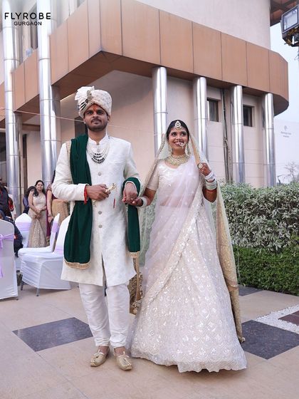 A beautiful shot of a couple on their wedding day. The groom wears a white sherwani with a contrasting green velvet stole, adding a touch of color and richness to the ensemble.