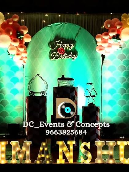 A colorful birthday stage with a mermaid-scale patterned backdrop, a rainbow balloon arch, and illuminated marquee letters for a bright and cheerful party.