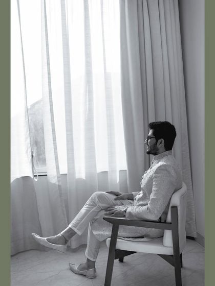 A pensive black and white portrait of the groom sitting by a window. It's a quiet, reflective moment captured just before he leaves for the ceremony.