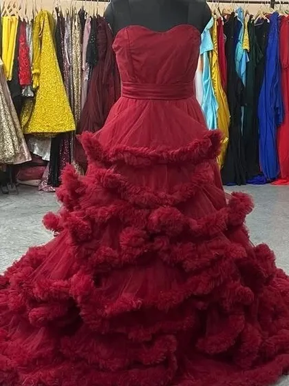 This wine-red ruffled gown is a showstopper. The strapless sweetheart neckline and dramatic, layered tulle skirt create a glamorous and unforgettable look, shown here on a mannequin in our showroom.
