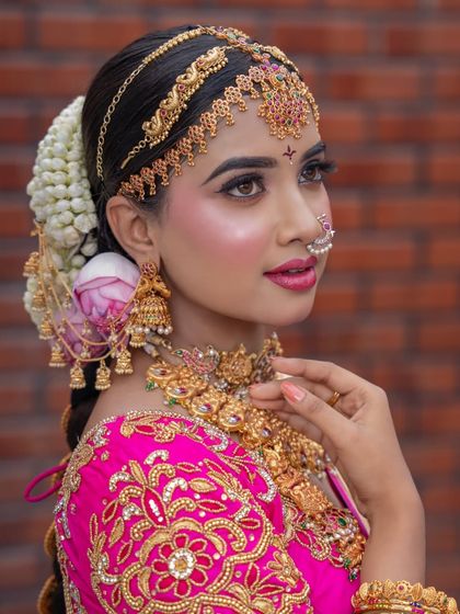 A close-up on the makeup and hair. The braided hairstyle is adorned with fresh flowers, and the makeup features a winged eyeliner and pink lips to match the outfit.