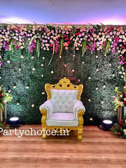 A classic and elegant floral stage suitable for a baby shower or a half saree ceremony. The design features a green wall backdrop with a lush floral border and a regal white throne.
