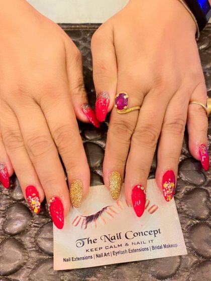 A stunning set of red almond nails perfect for a festive occasion. The design includes gold glitter accent nails and abstract art with gold foil and colorful specks.