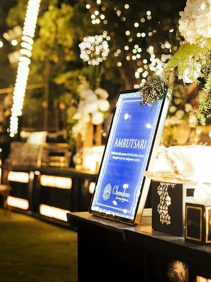 An elegant, backlit sign for the 'Amritsari' food station at an outdoor evening event, creating a beautiful and inviting glow.
