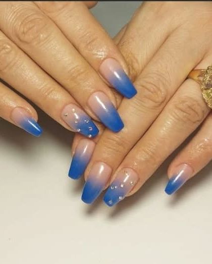 A beautiful set of long, coffin-shaped nails with a blue ombre effect and scattered rhinestones that look like little stars.