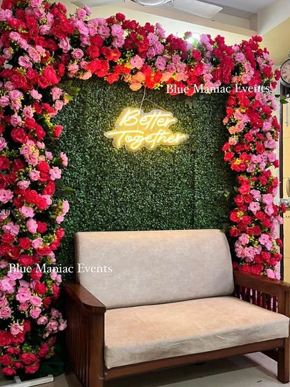 A 'Better Together' backdrop perfect for an anniversary celebration. The design features a green wall framed by an arch of red and pink flowers and a neon sign.