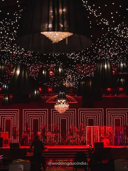 A stage designed to steal the spotlight under an indoor night sky. The combination of a starry ceiling, dramatic red geometric lighting, and crystal chandeliers created a magical and moody setting for the sangeet performances.