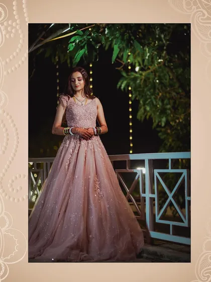 A stunning full-length portrait of the bride on her reception night. She stands on a balcony, framed by fairy lights, looking every bit the princess in her beautiful pink gown.
