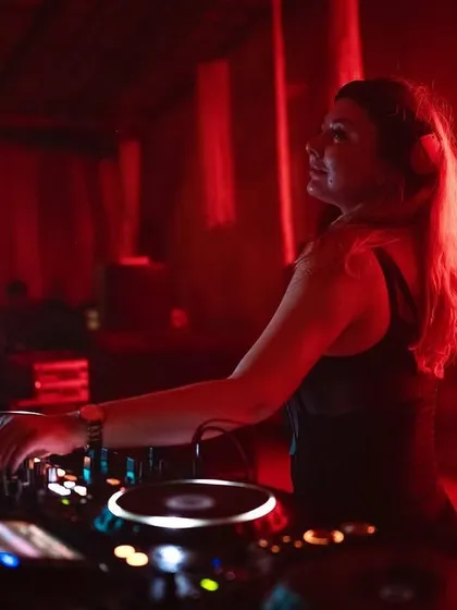 In the red-lit DJ booth at Aura, focused on the mix. The neon lights create a classic club vibe.