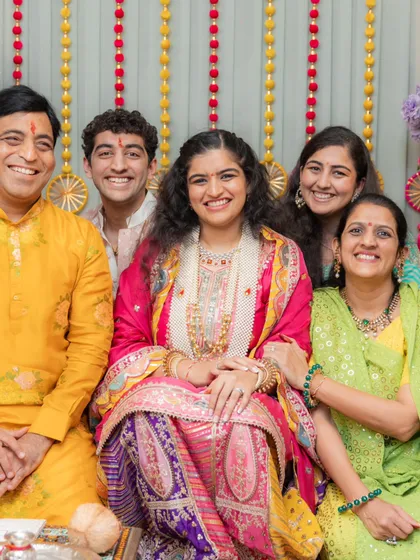 A lovely family portrait from the Bane Bithai ceremony. The bride is radiant in a multi-colored outfit, and her family is coordinated in bright, festive colors like yellow, green, and pink, creating a picture full of warmth and joy.