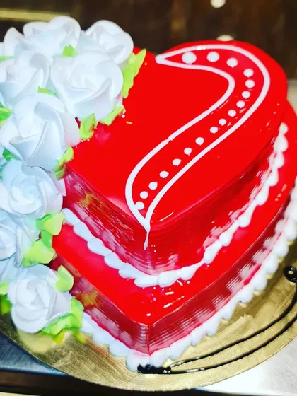 A classic and vibrant heart-shaped cake with a glossy red finish. Adorned with a cascade of delicate white buttercream roses, this cake is a timeless expression of love.