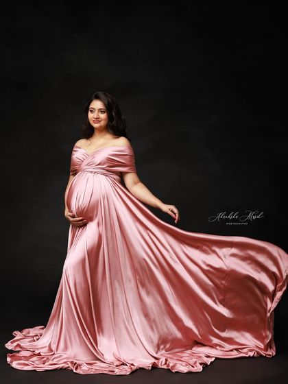 The flowing pink satin gown against a dark backdrop creates a dramatic and timeless portrait that is pure elegance.