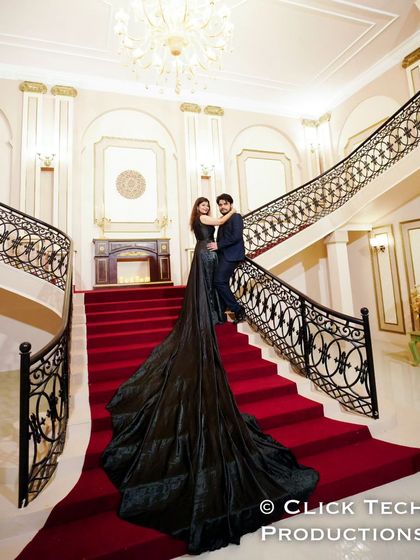 A full view of the couple on the grand staircase, showcasing the impressive length of the black trail gown and the luxurious setting.