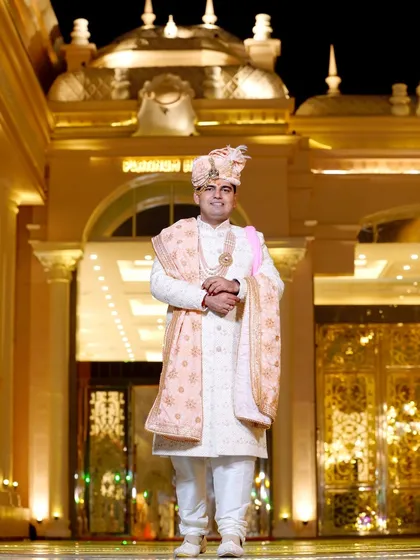 A grand portrait of the groom in his magnificent sherwani, standing before the beautifully lit wedding venue. A truly royal shot.