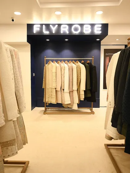 A clean, well-lit view of our store's interior, with our signature blue wall and a rack of our latest ivory and pastel sherwanis.