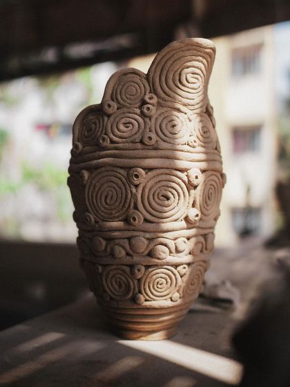 This intricate vase was made entirely using the coil-building technique. Each coil is rolled and layered by hand to create the swirling patterns that cover the surface.