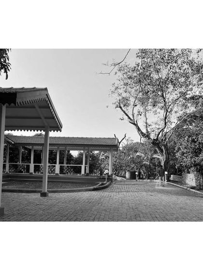 A black and white photograph emphasizing the textures of the heritage site. The aged cobblestone driveway and the intricate details of the pavilion's roofline speak to a design that respects the passage of time.