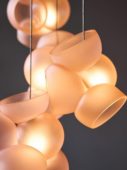 A close-up of the Bocci 100 series in a warm, amber-pink hue, highlighting the soft texture and inviting glow of the hand-blown glass.