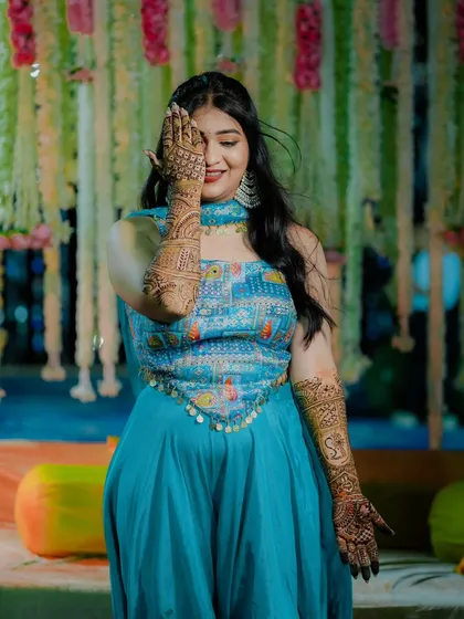 A playful bride covers one eye with her mehndi adorned hand, a fun and charming portrait from her Mehndi ceremony.