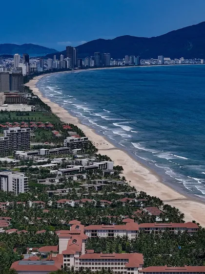 The stunning coastline of Da Nang, Vietnam. The long sandy beach is lined with resorts and hotels, with mountains in the background.