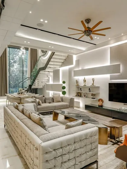 This living room at the H-360 Vikaspuri residence is a perfect example of modern luxury. The space features a mix of leather and fabric sofas, a statement orange armchair, and a custom media wall with integrated shelving.