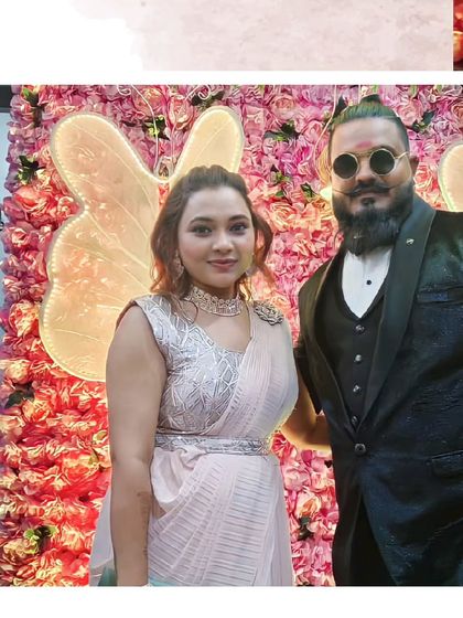 This couple is ready for the party. He is rocking a stylish black tuxedo with a man-bun, and she is elegant in a light pink belted saree.