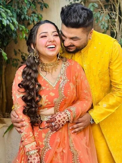 A joyful moment from a Haldi ceremony. The groom's bright yellow kurta with a long mirror-work jacket is the perfect festive attire for this happy occasion.