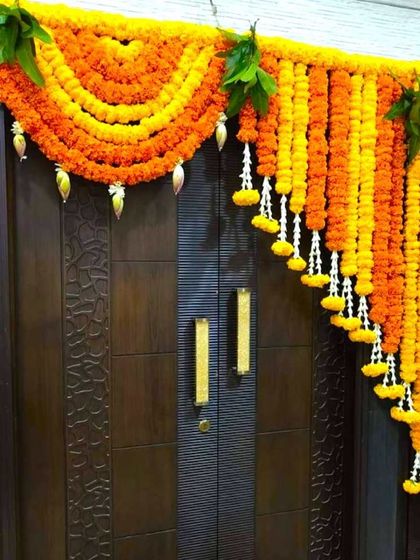 A traditional Griha Pravesh decoration for a main door. The arch is made of marigold garlands with hanging bell and leaf accents.
