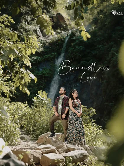 A stunning wide shot of a couple standing on rocks in a lush forest, with a waterfall in the background, titled 'Boundless Love'.