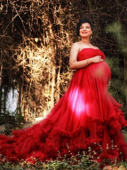 The sheer tulle of this red maternity gown catches the light beautifully, highlighting the baby bump. It's a radiant and joyful look for any expecting mother.