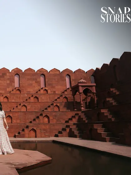 A wide-angle shot capturing the bride against the vast and intricate architecture of a historic step-well, creating a sense of awe and grandeur.