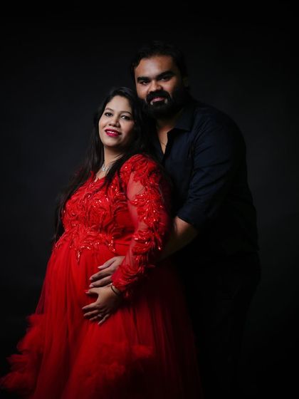 An intimate couple portrait against a dark background. The vibrant red of the gown stands out, creating a romantic and powerful image of togetherness.