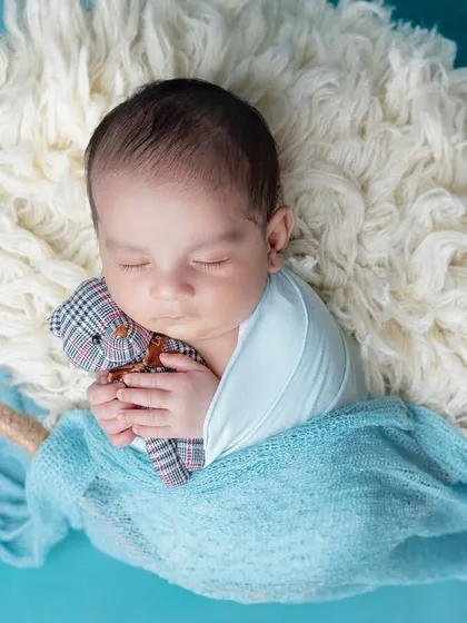 A baby boy cuddles a tiny teddy bear while sleeping in a basket.