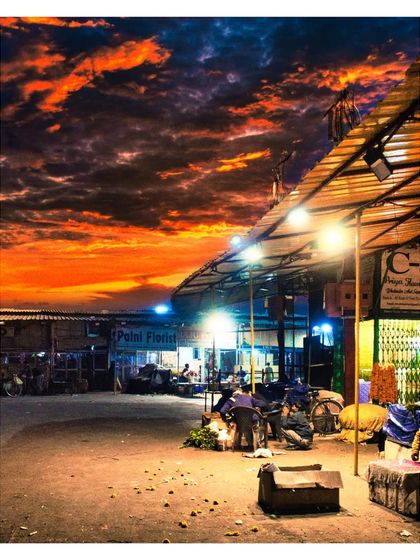 A wide shot of the Phool Mandi at dusk, with a fiery orange sky contrasting against the illuminated market stalls. This image showcases our skill in landscape and architectural photography within a street setting.