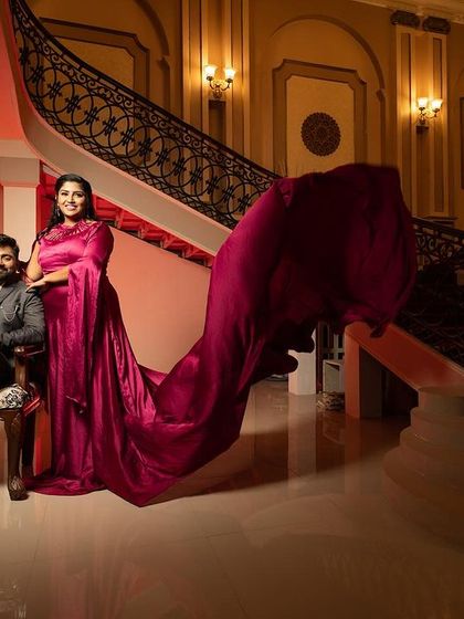 A regal portrait in a mansion-like setting, with the groom seated and the bride standing, her magenta trail gown adding a touch of royal elegance.