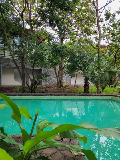 The turquoise pool at 'Villa 16' contrasts with the grey stone walls and green foliage. The material and color palette is inspired by the natural surroundings.