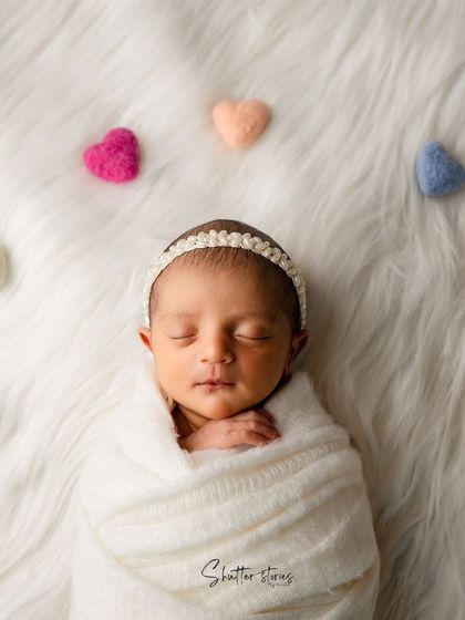 A classic and pure setup with a newborn in a white swaddle on a fluffy white blanket, surrounded by colorful felt hearts.
