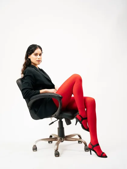 A full-length shot of the model in an office chair, blending corporate and high-fashion aesthetics. The pose is confident and relaxed, making a strong statement.