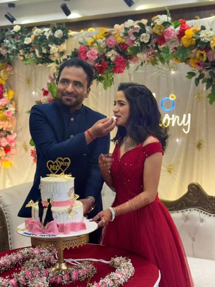 A sweet moment of celebration. The groom-to-be feeds his partner a piece of cake at their ring ceremony, where she is wearing a beautiful red gown.