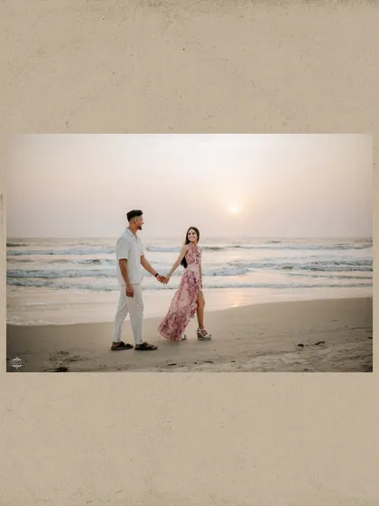 A wide shot of a couple taking a romantic walk along the shoreline at sunset. This photo emphasizes the beautiful scenery of a destination beach photoshoot.