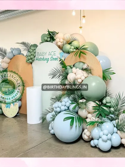 A "Baby Ace Hatching Soon" dinosaur-themed baby shower. The decor features egg props, tropical leaves, and a beautiful balloon arrangement in muted greens and blues.