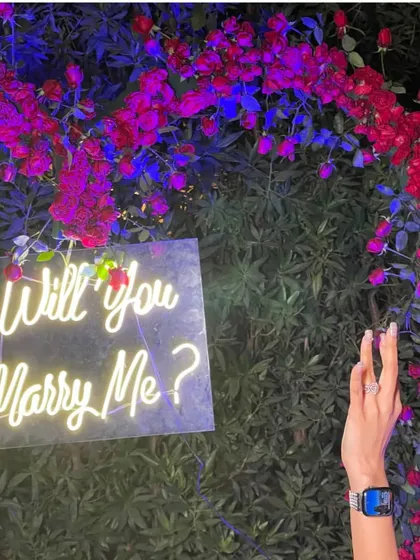 A close-up of the "Will you Marry Me?" neon sign, which adds a modern and personal touch to this beautiful garden proposal setup.
