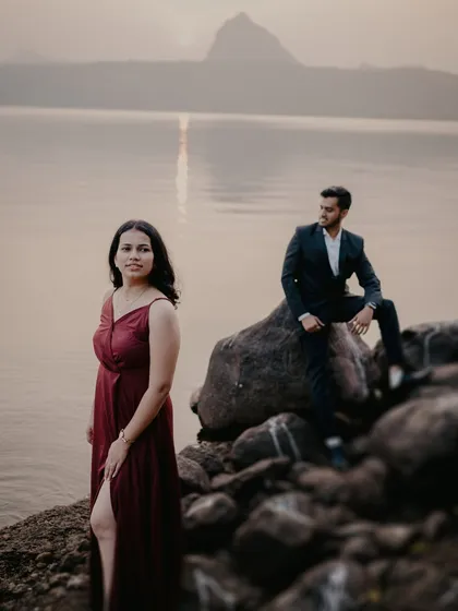 A dramatic, wide-angle shot with the bride in the foreground and the groom perched on a rock behind her. The mountain in the distance adds a majestic feel to this Pune pre-wedding location.