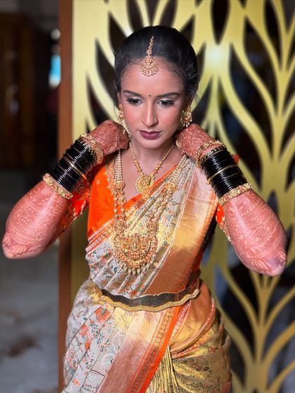 Adjusting the final details. This pose highlights the stunning temple jewellery and the rich texture of the silk saree, key elements of a classic South Indian bridal look.